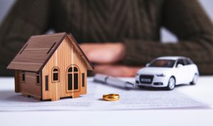 small model of a home and vehicle on top of paperwork next to a wedding band and pen