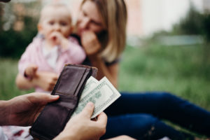 man pulling money out of his wallet in front of wife and baby