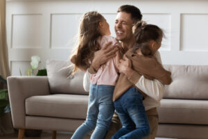 cheerful happy young adult dad embracing cute kids daughters cuddling at home