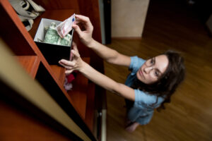 a girl puts or takes dollars from a money-box on the top shelf of a closet