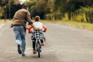 rear view of a boy riding a bicycle while his father runs along holding the kid